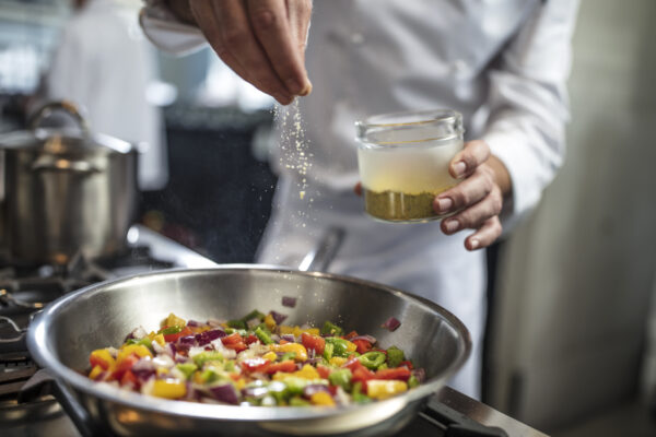 Chef seasoning pan of vegetables on stove in the hotels restaurant kitchen